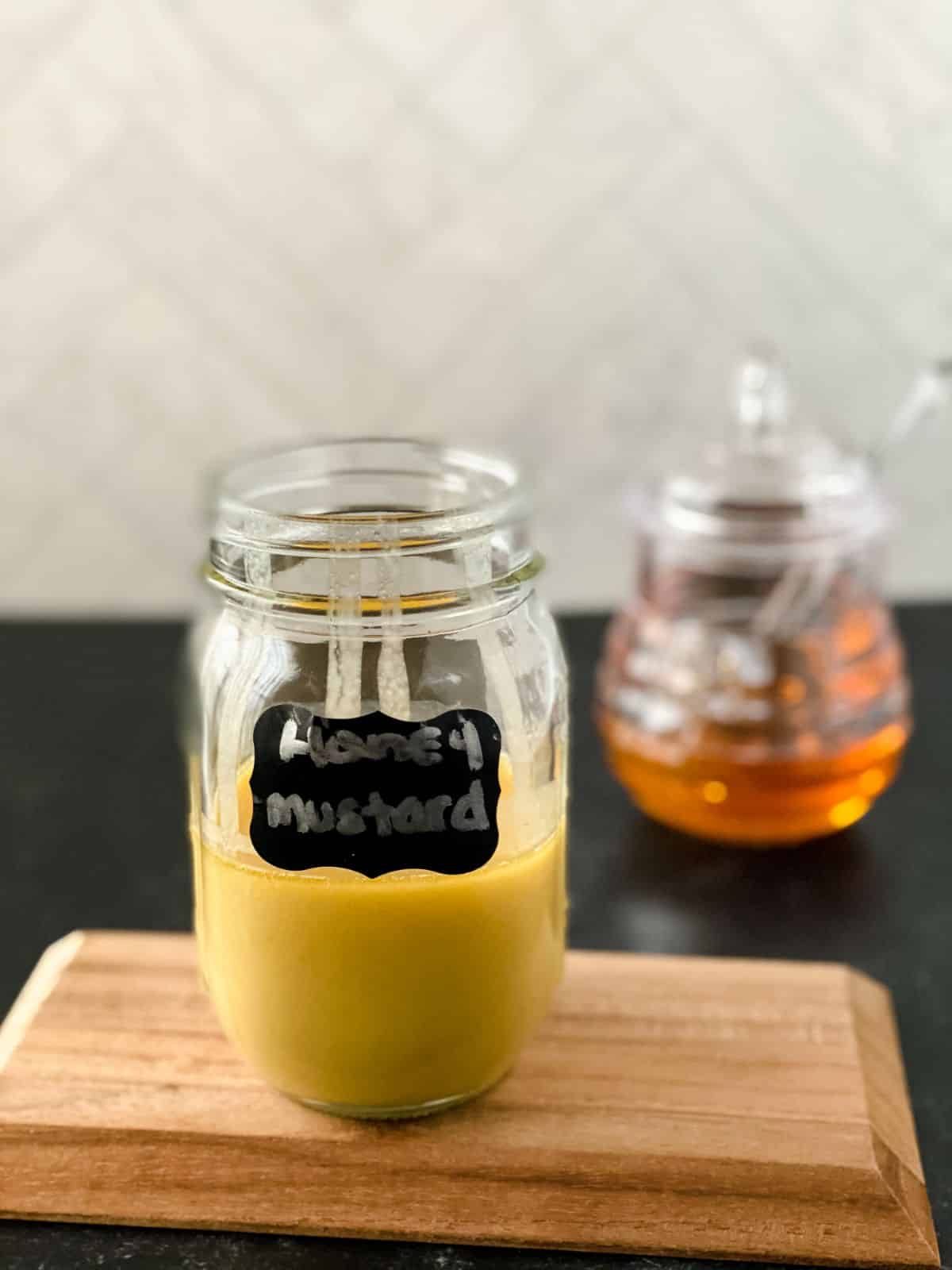 homemade honey mustard in a mason jar on black counter with honey in glass jar in background