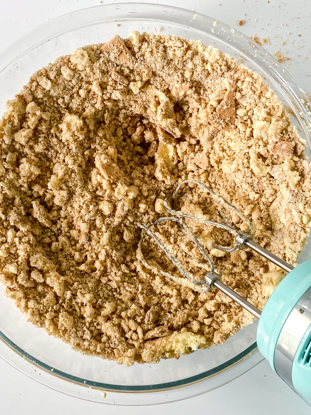 teal hand mixer in bowl with graham cracker crumbs and butter
