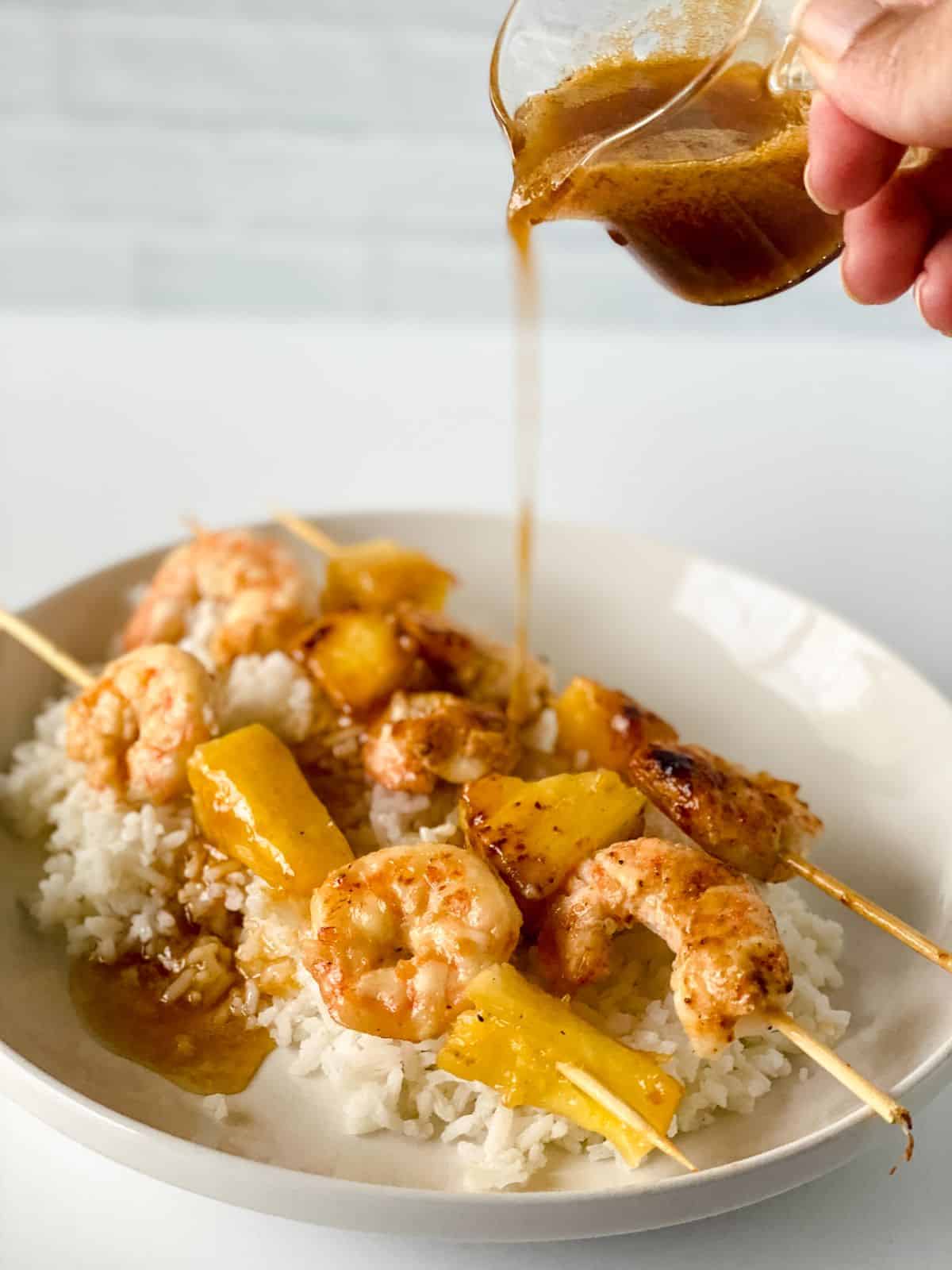 sauce being poured over pineapple shrimp skewers