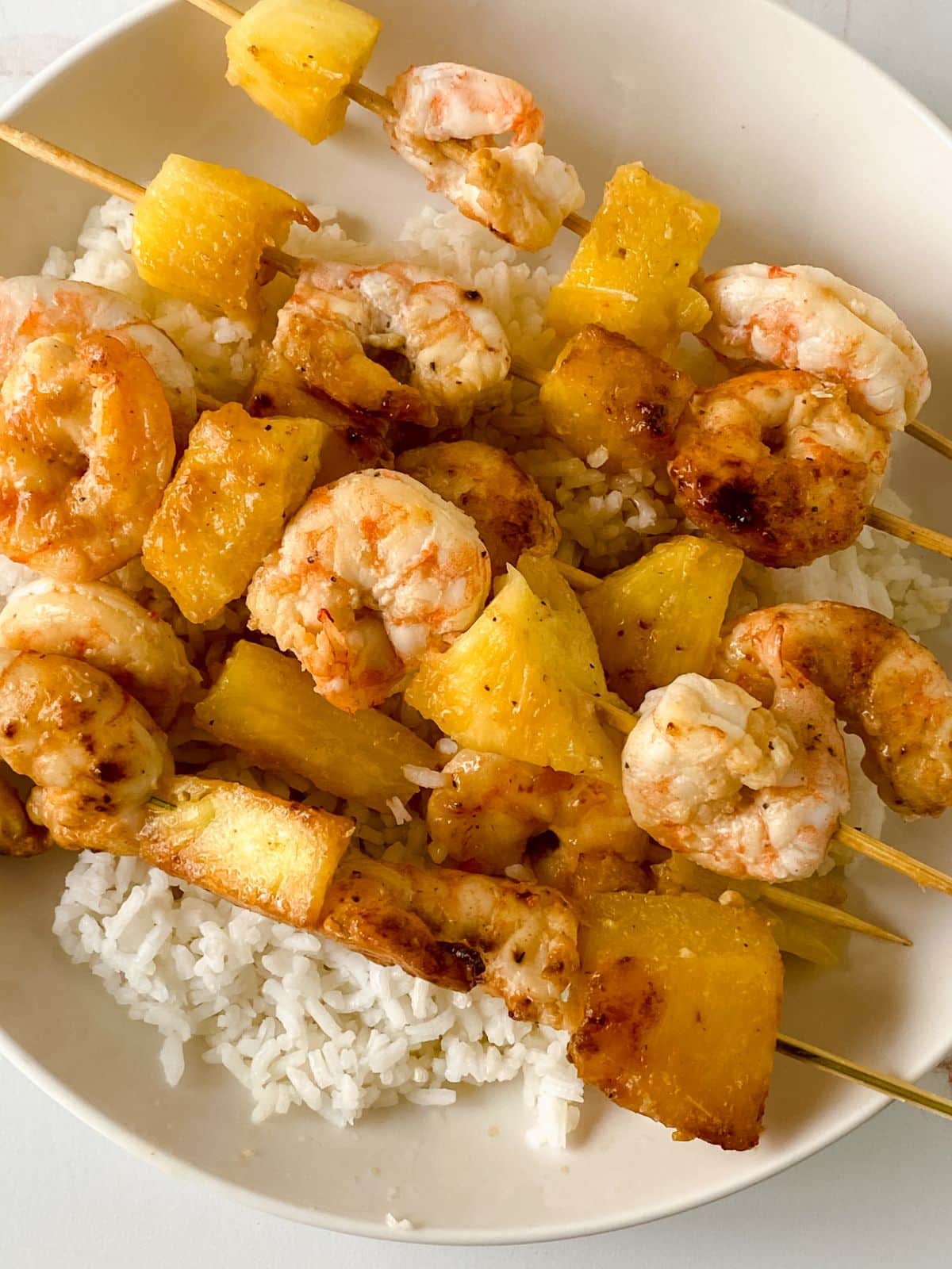 plate of rice topped by shrimp and pineapple skewers