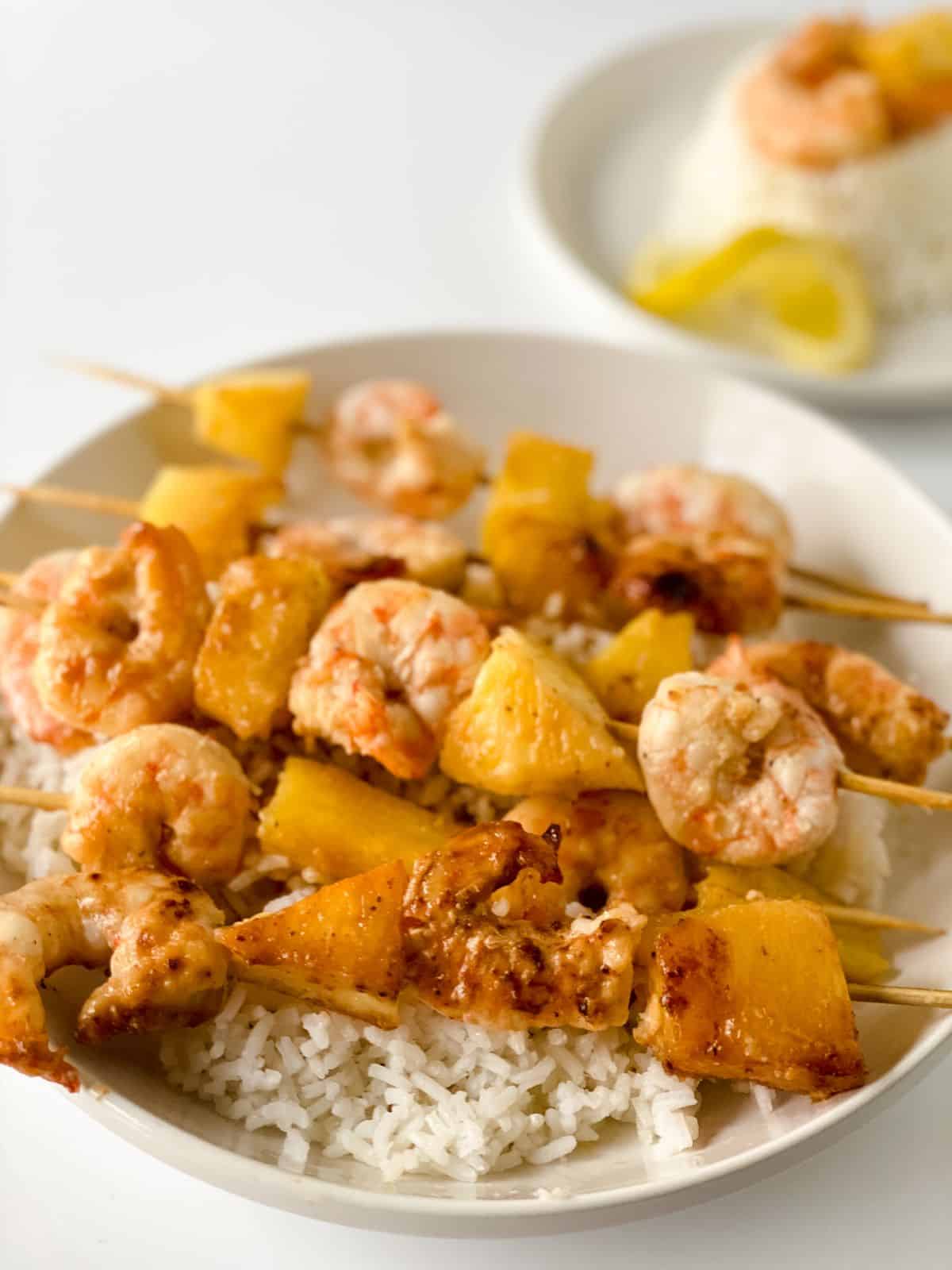 white rice beneath pineapple shrimp kabobs on white plate