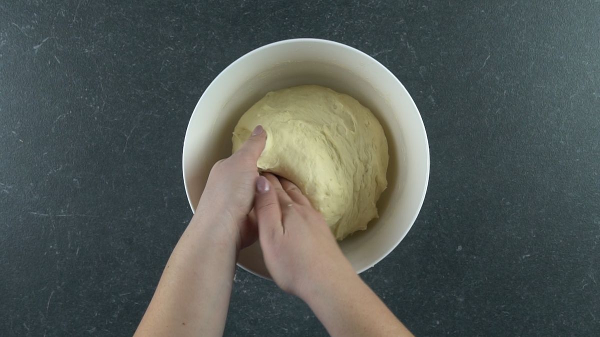 hands putting ball of dough into white bowl to rise