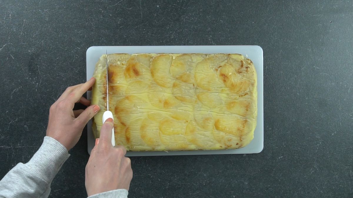 knife cutting pave potato on white cutting board