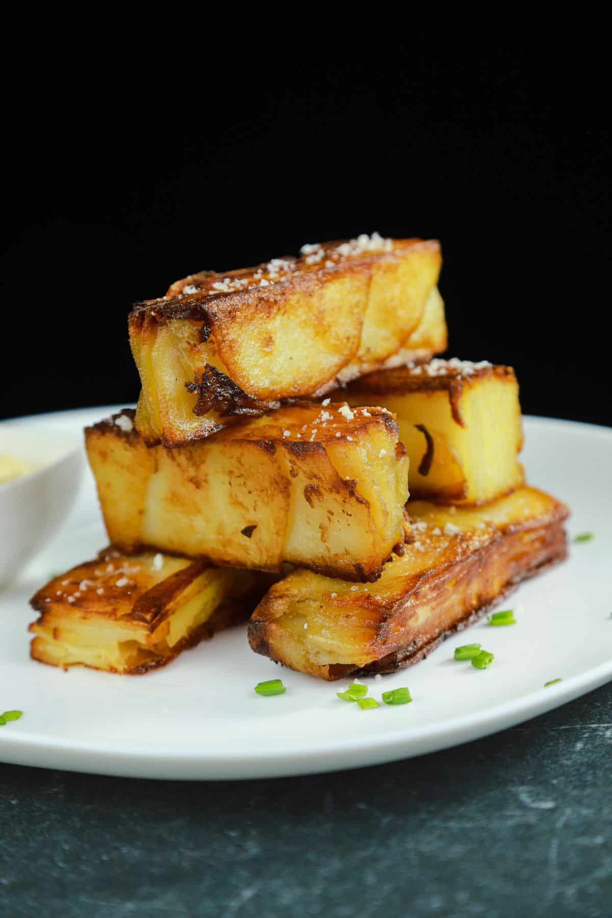 stack of fried potato sticks on white plate with black background