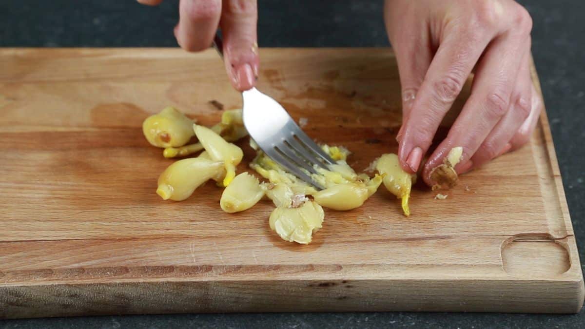 fork mashing garlic on cutting board