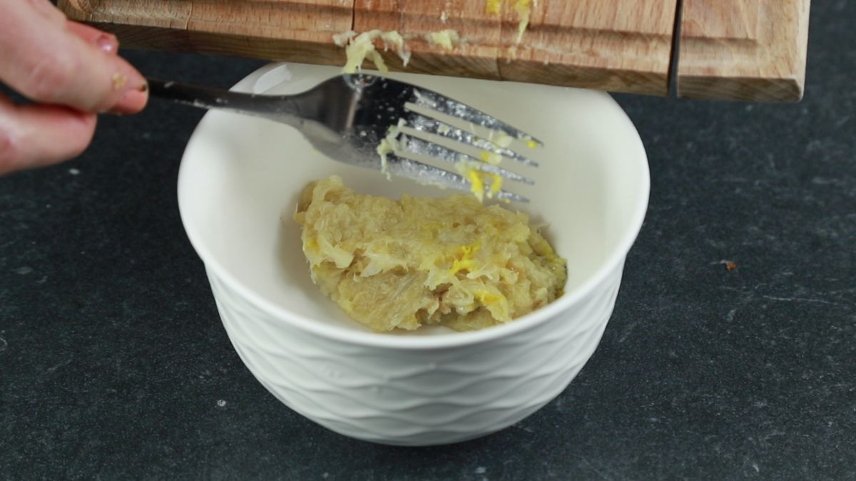 mashed garlic being scraped into white bowl