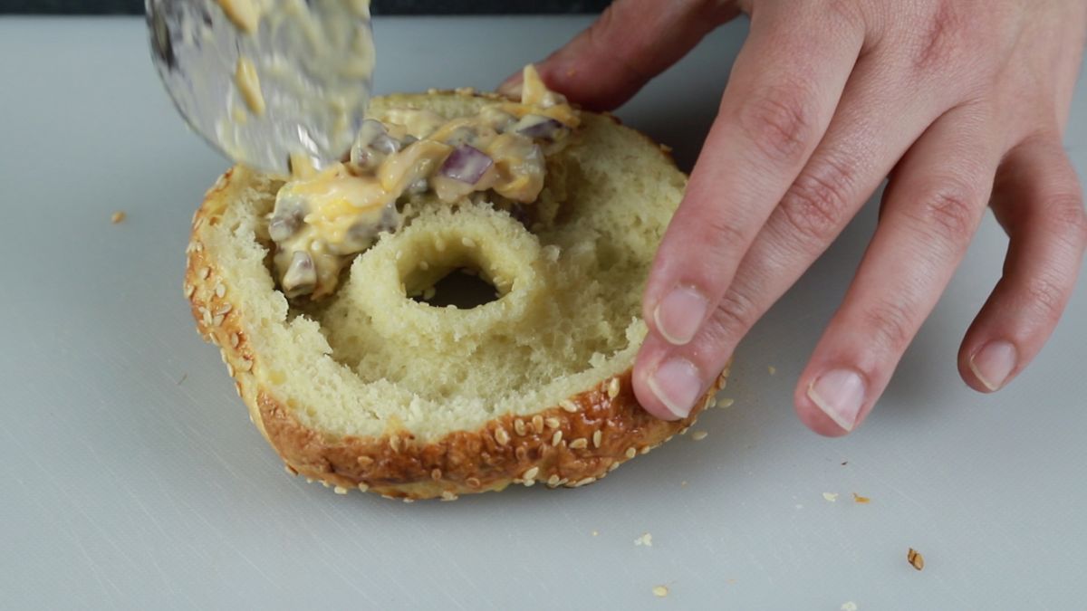 spoon adding quiche filling to bagel halve