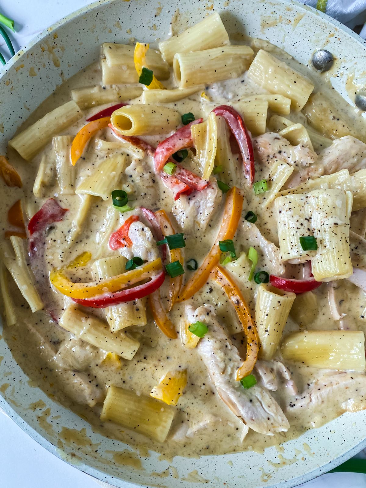 white skillet of pasta in cream sauce with bell peppers