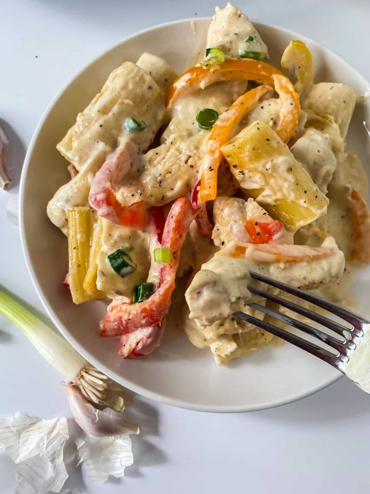 fork holding pasta above white bowl