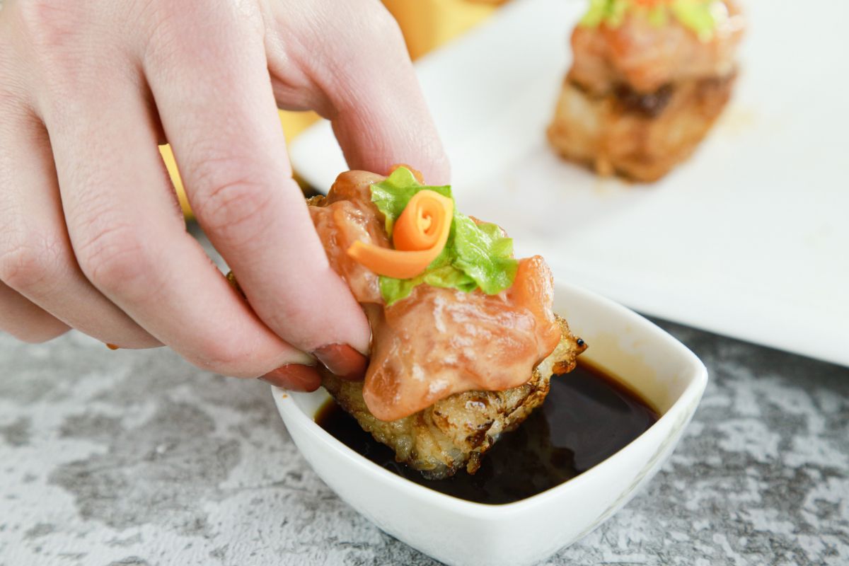 hand holding rice with salmon sushi in soy sauce