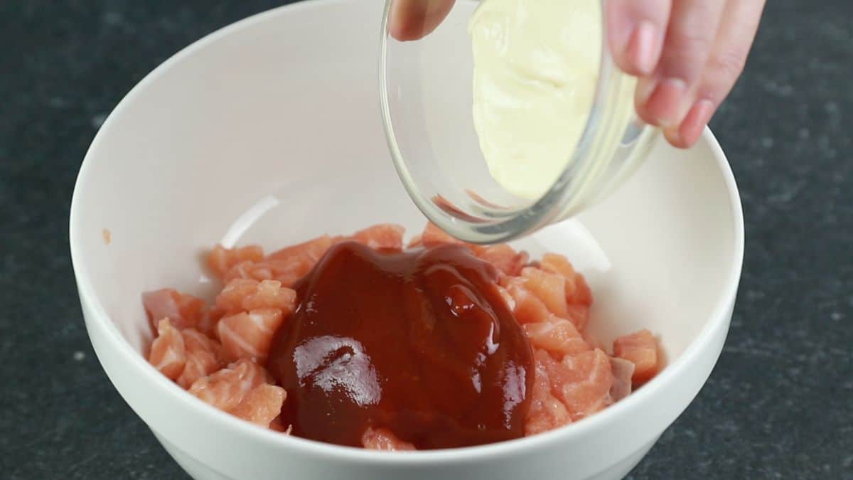 mayonnaise being poured on top of bowl of chopped sushi