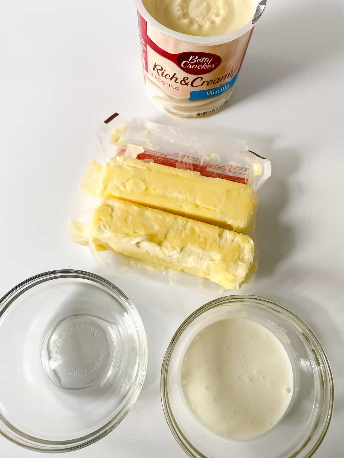 two sticks of butter next to container of frosting on white table