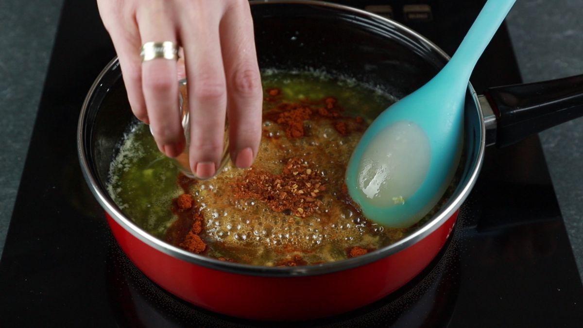 adding spices to spicy honey garlic chicken in skillet with blue spoon