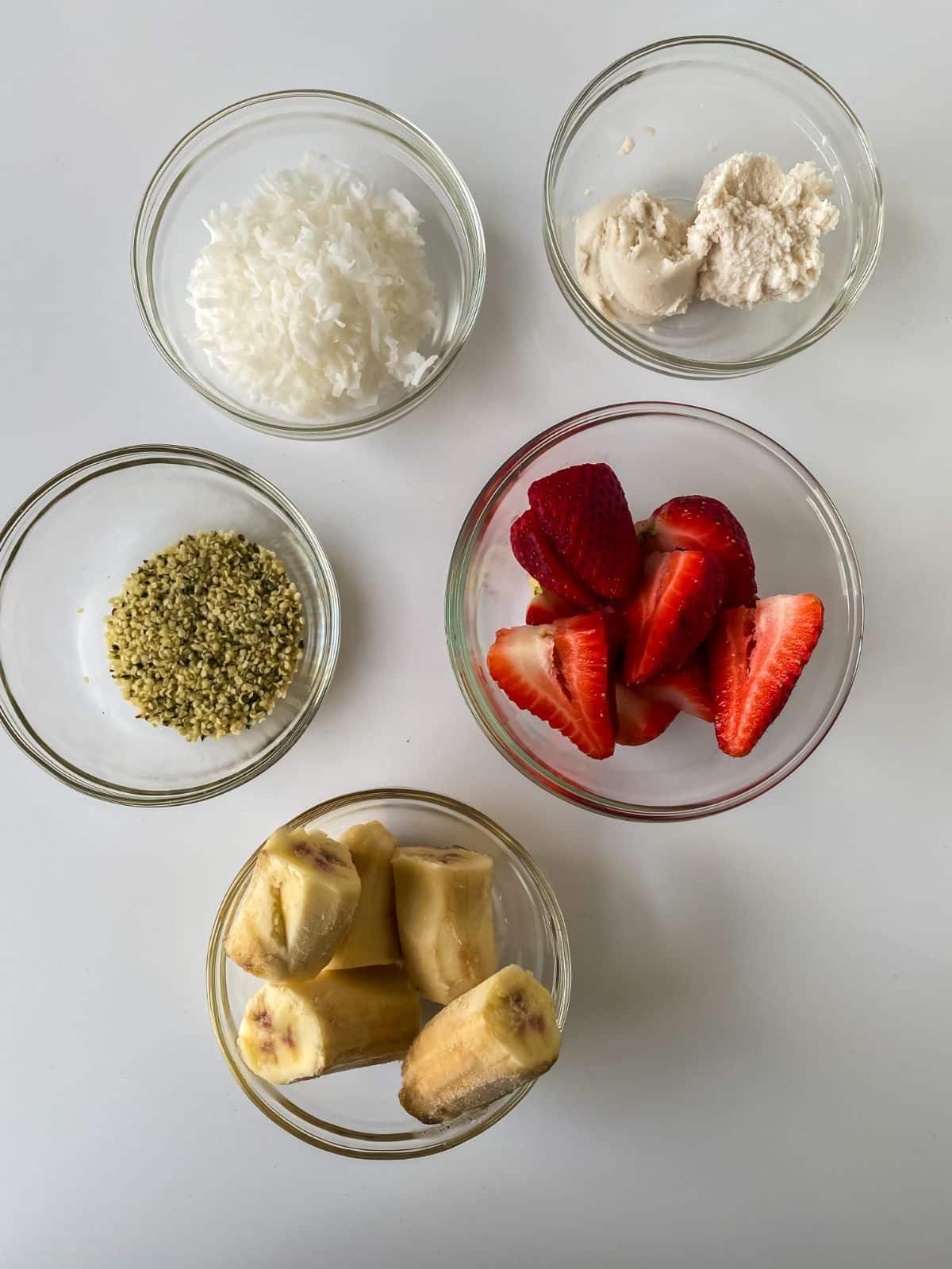 glass bowls of bananas strawberries and coconut on white table