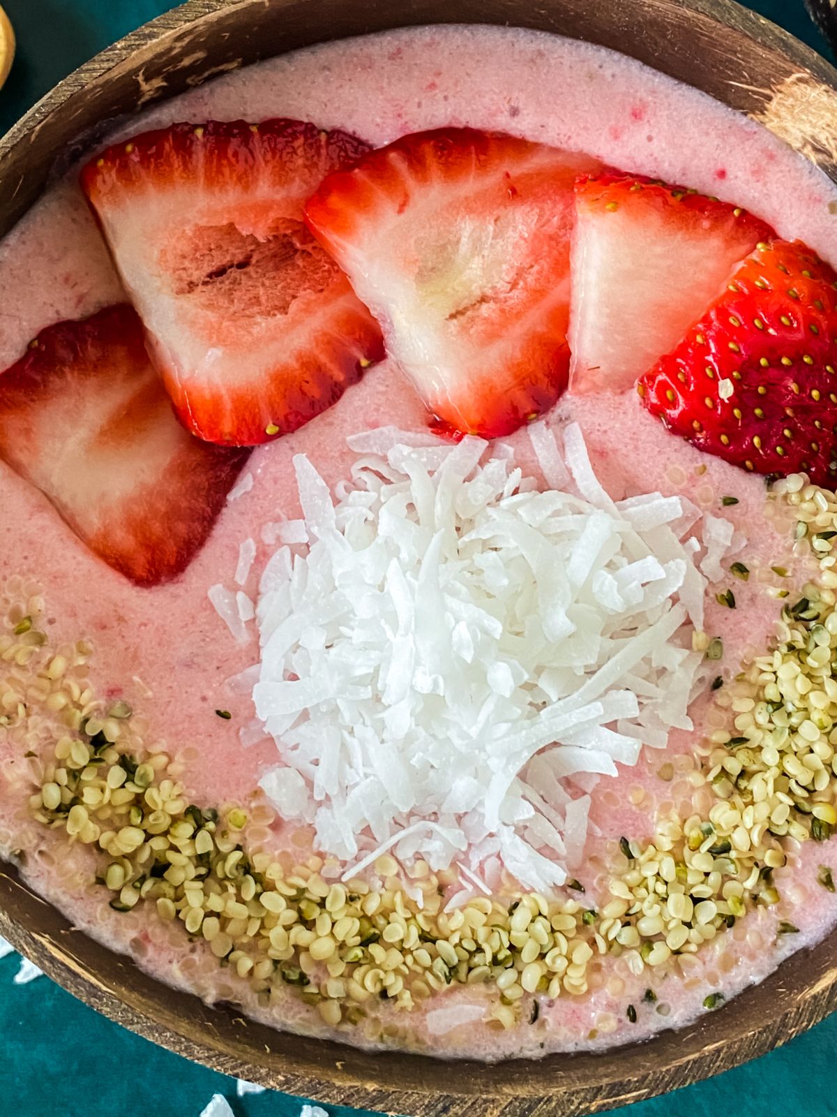 wood bowl of smoothie topped by coconut and sliced strawberries