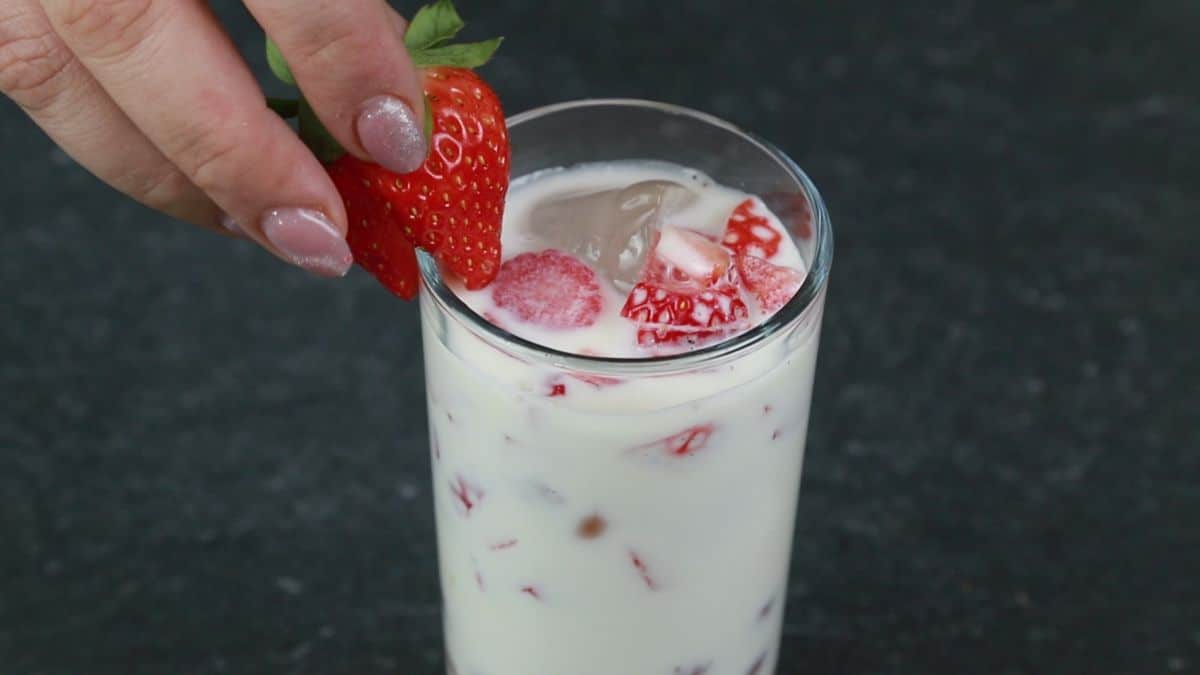 strawberry being put on edge of glass of boba milk