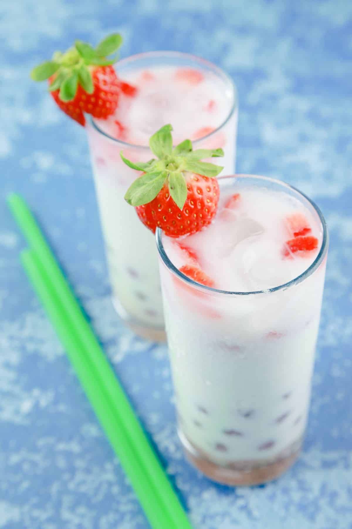 two tall glasses of strawberry boba milk on blue table