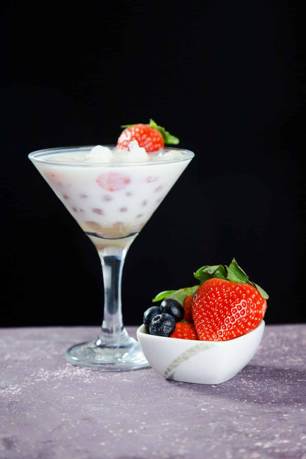 strawberry pieces on top of boba milk in martini glass on gray table