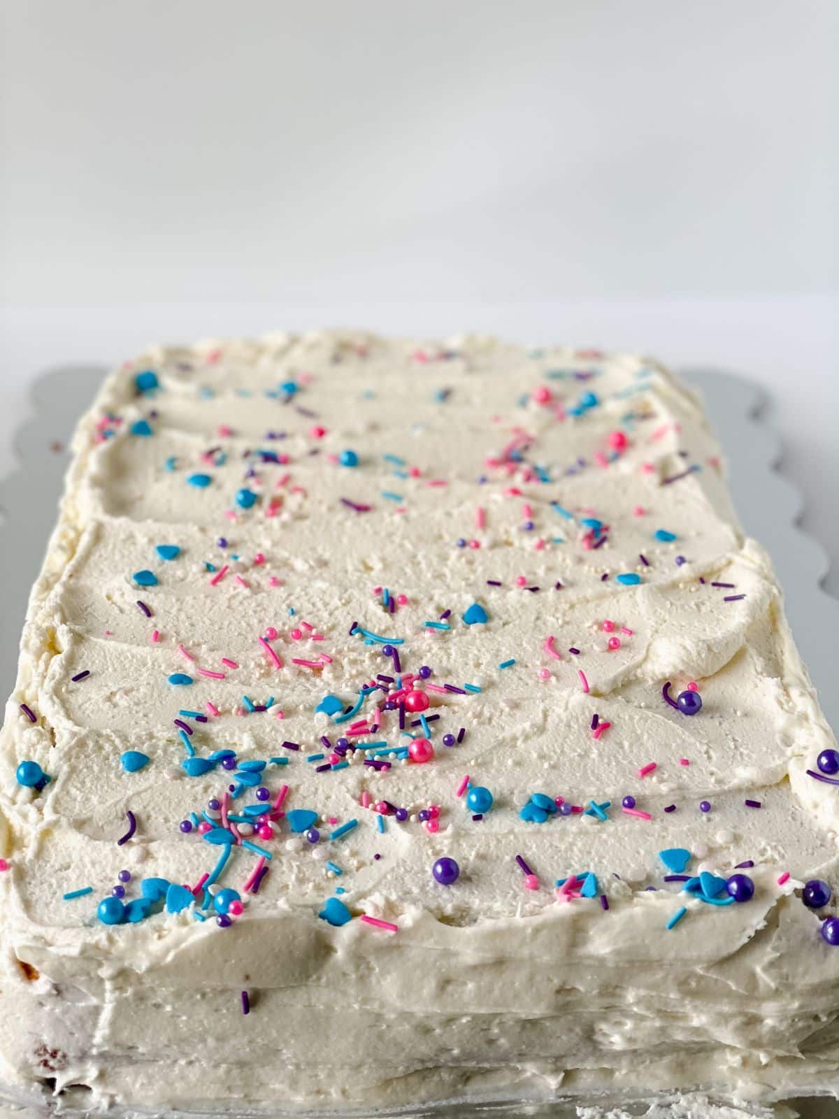 vanilla sheet cake on tray with white icing and blue and pink sprinkles