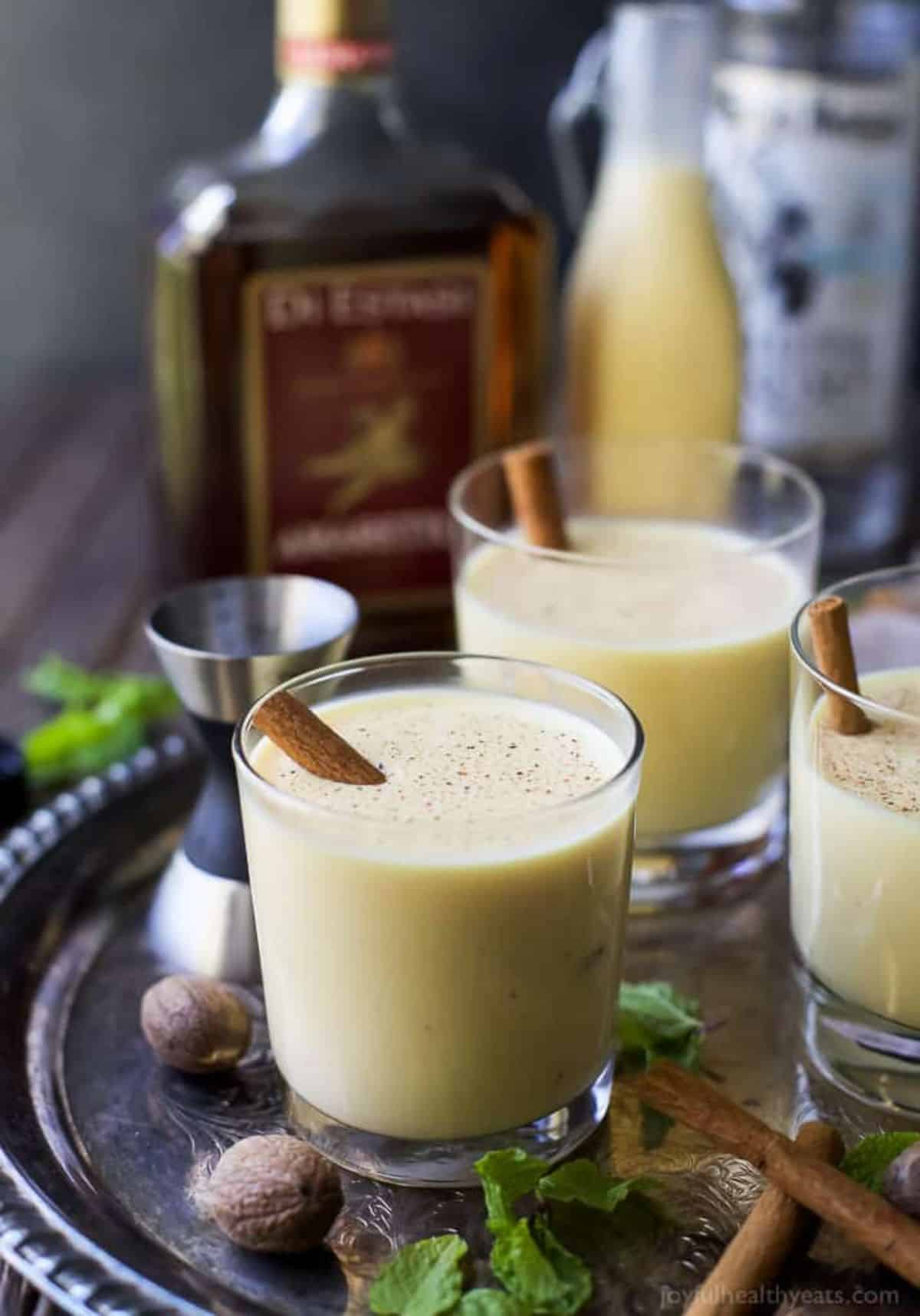 Spiked Eggnog rum cocktails in glass cups with cinnamon sticks on a metal tray.