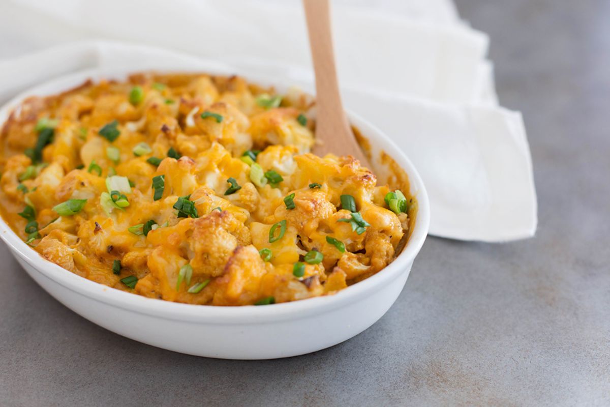 Low-Carb Cauliflower Mac and Cheese in a white bowl with a wooden spatula.