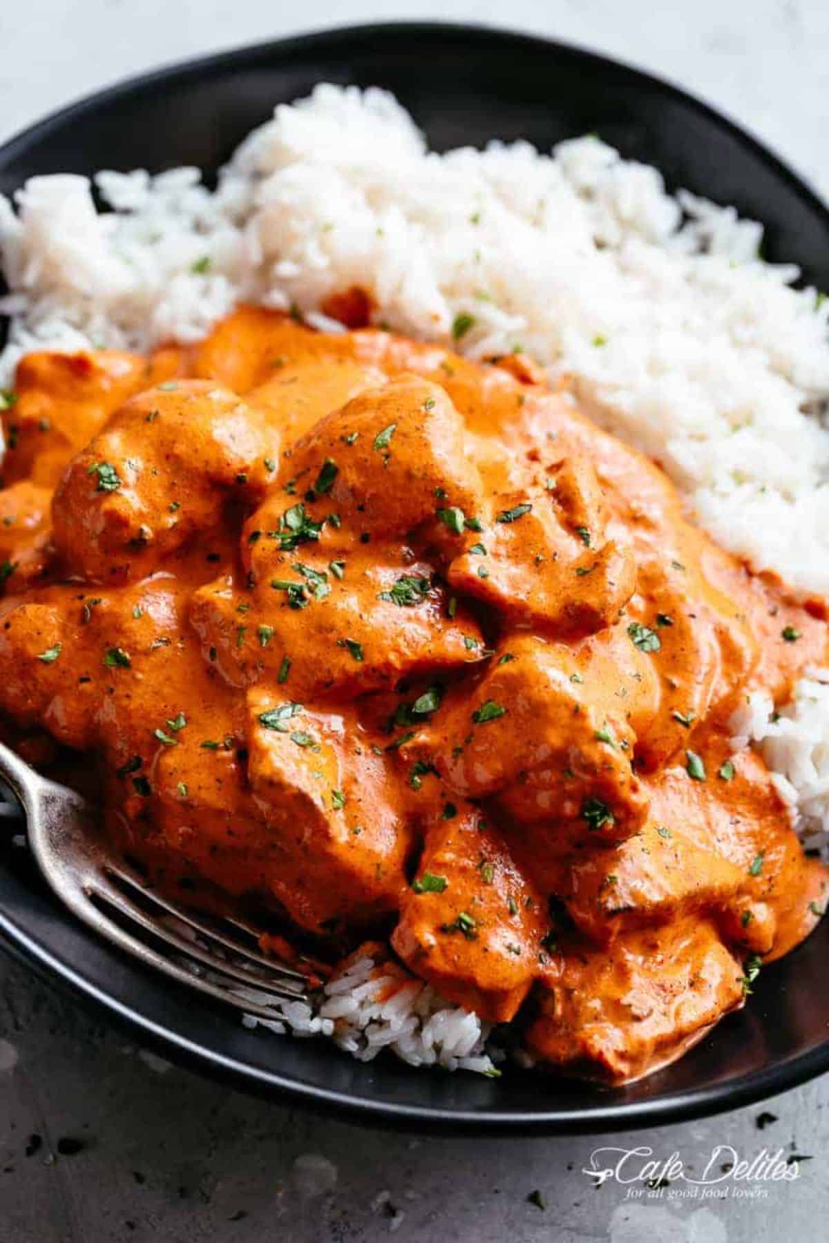 Butter Chicken on a black plate with a fork.