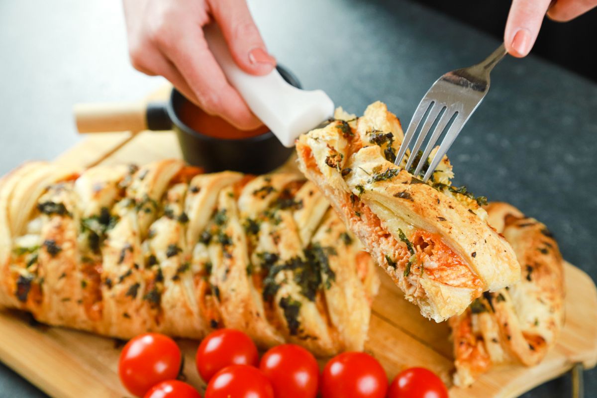 knife and fork holding slice of chicken braid above cutting board