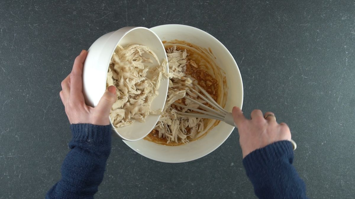 shredded chicken being added to bowl of sauce