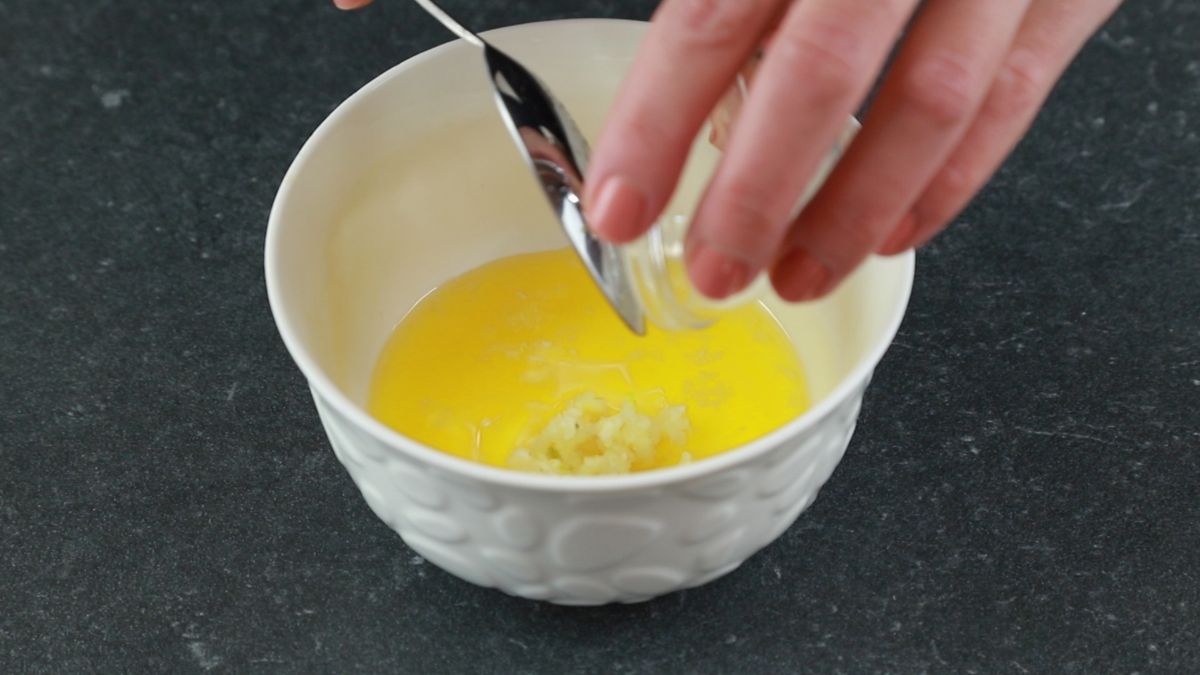 garlic being added to white bowl of melted butter