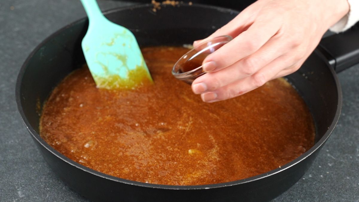blue spatula stirring vanilla into caramel in skillet