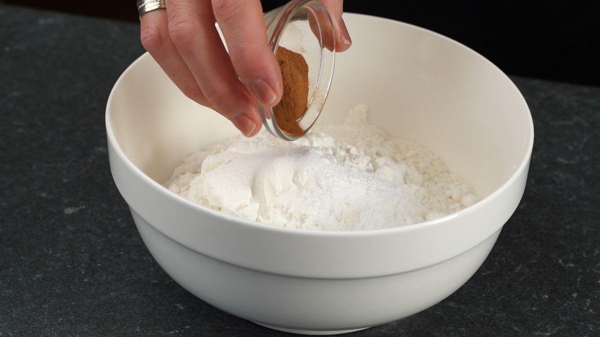 cinnamon being added to white bowl of flour