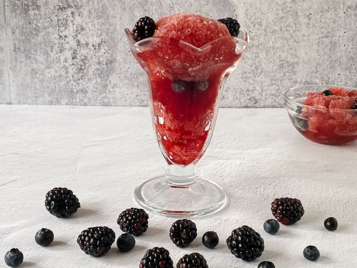 tall ice cream glass filled with blackberry wine sorbet on white table next to fresh berries