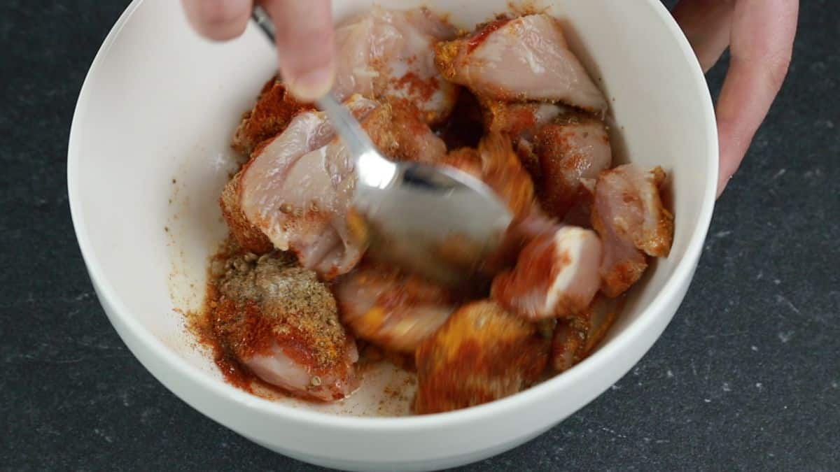 stirring chicken with seasonings in white bowl