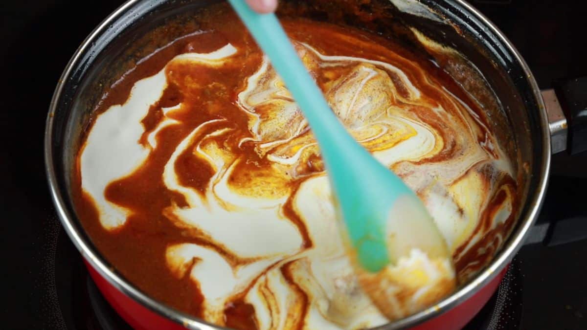 cream being stirred into butter chicken sauce in saucepan