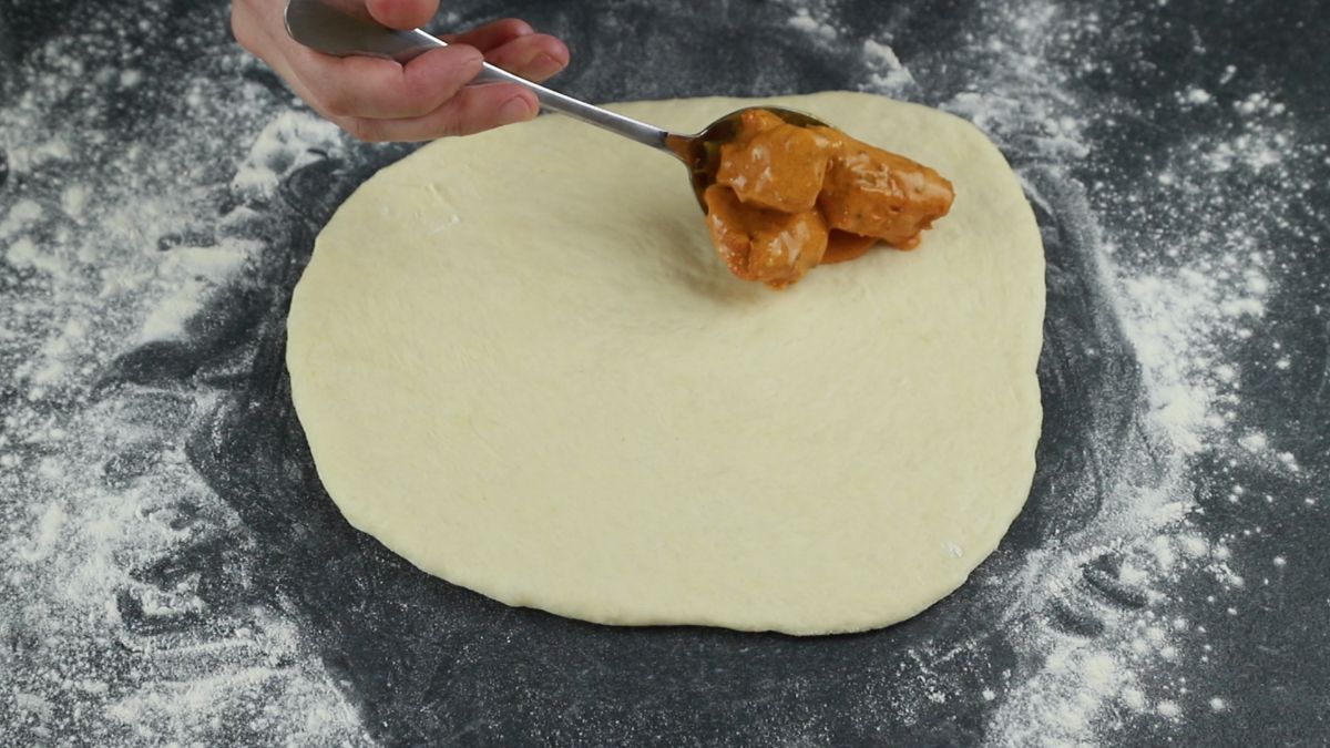 chicken and sauce being laid on top of calzone dough