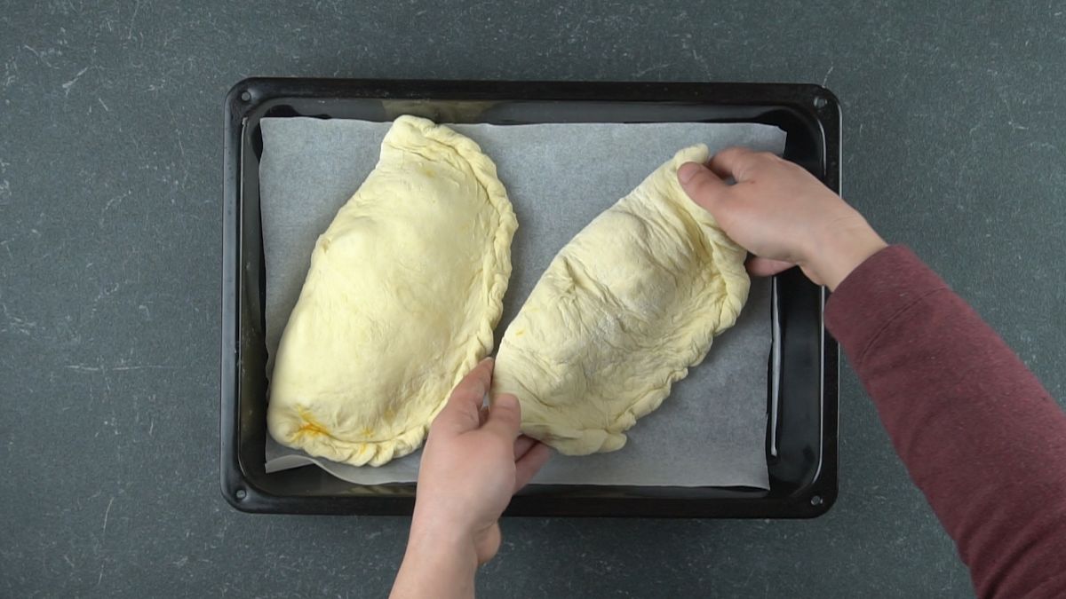 two unbaked calzones on baking sheet