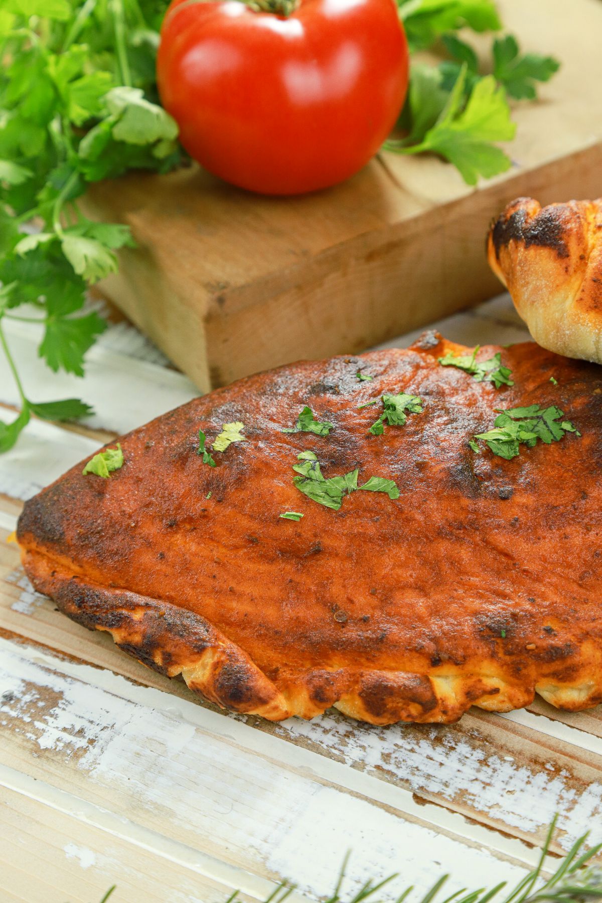 calzone on table by wood cutting board and tomatoes