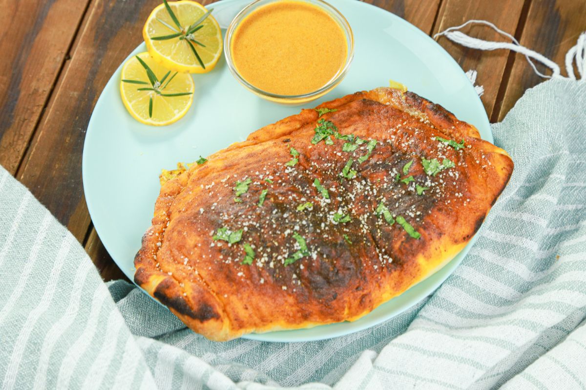 striped napkin on wood table by blue plate of butter chicken calzone