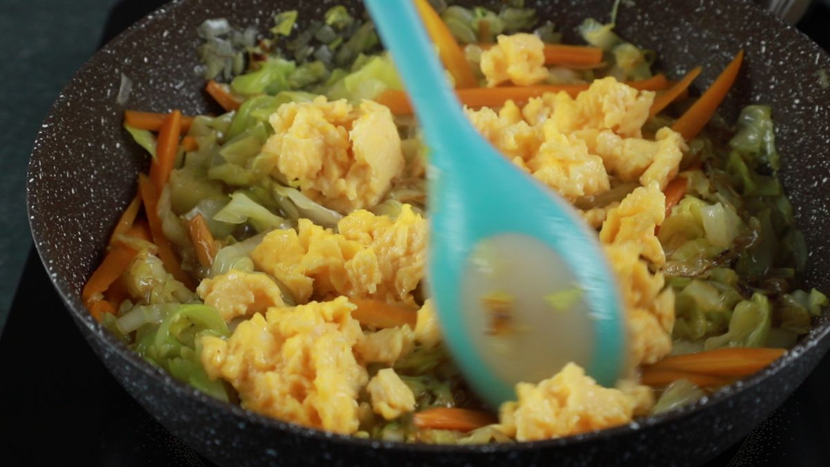 blue spoon stirring eggs into cabbage