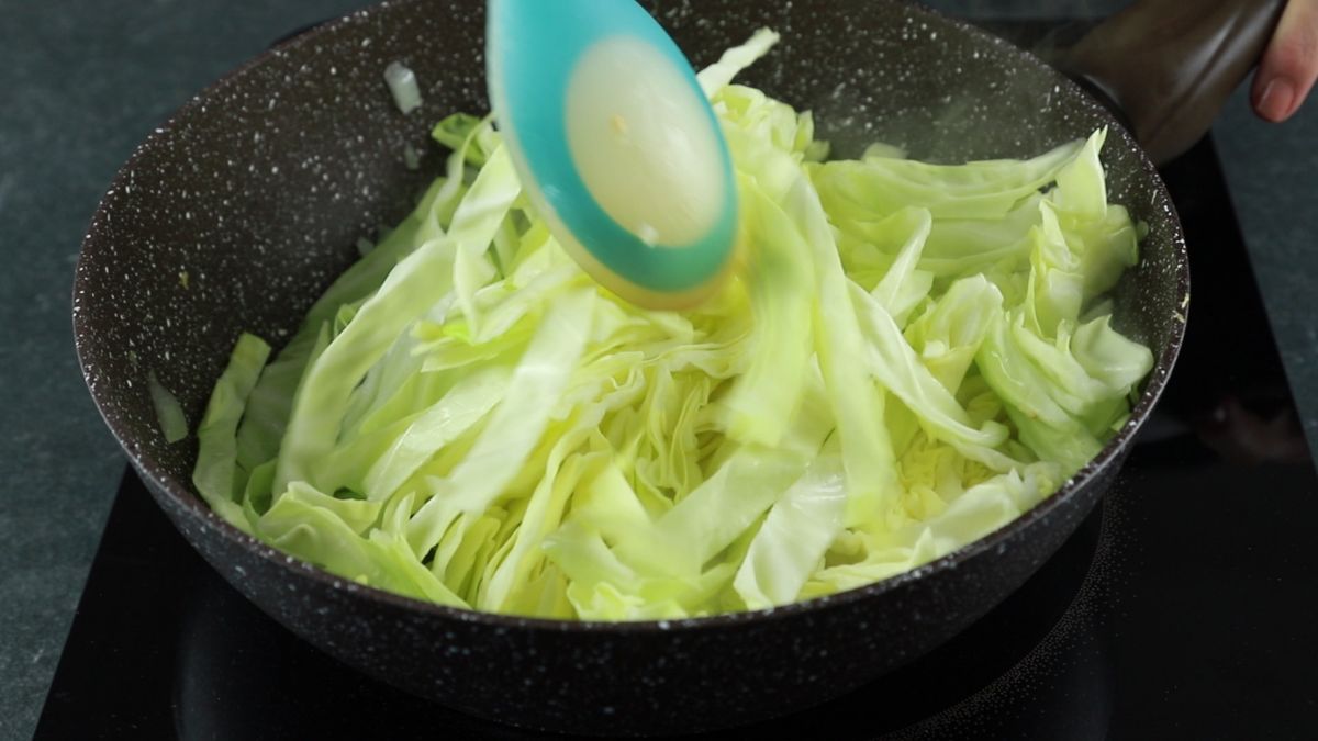 blue spoon stirring cabbage in black skillet