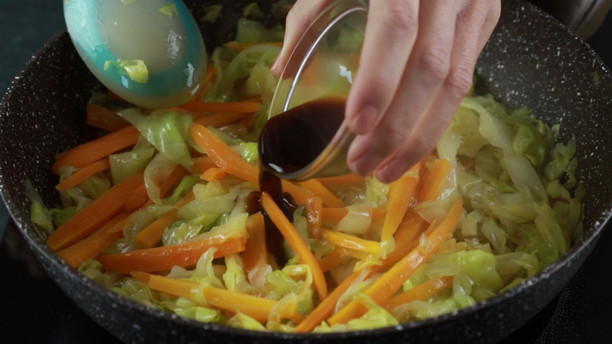 soy sauce being poured into skillet of cabbage and carrots