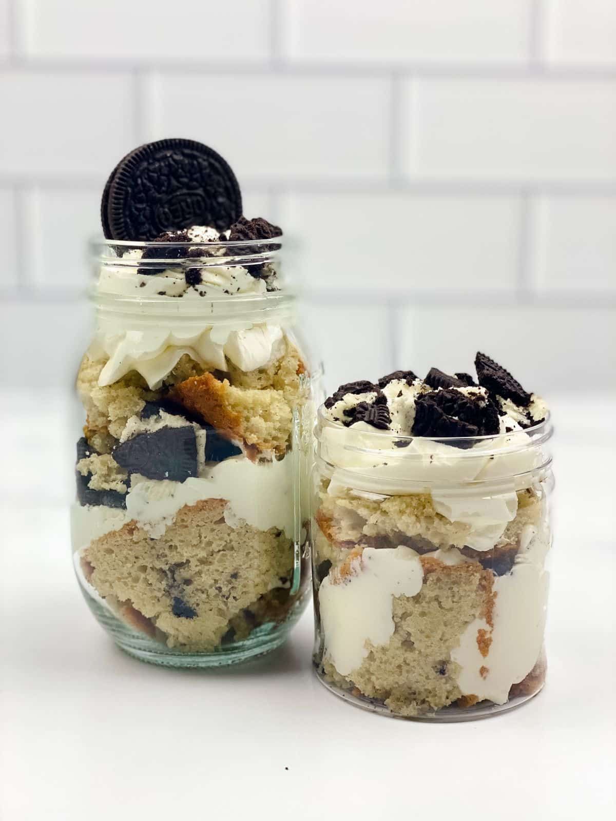 two mason jars filled with cake and cookies on white counter with white brick background