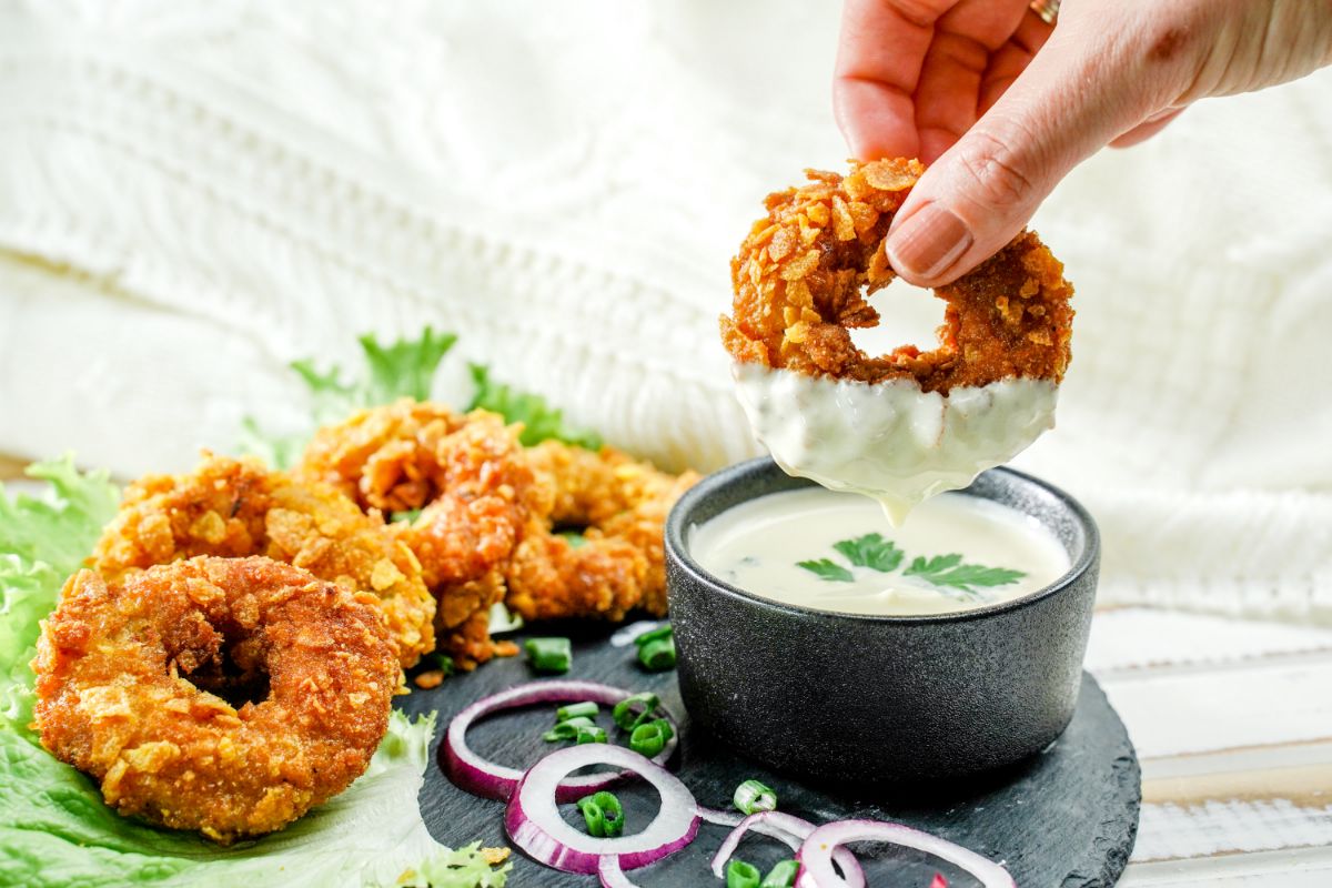 hand dipping chicken ring into sauce