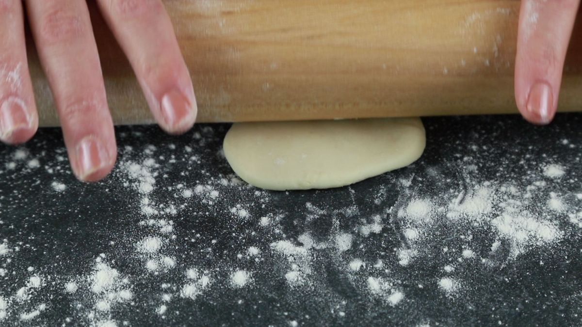 wonton wrapper being rolled out on black surface with flour