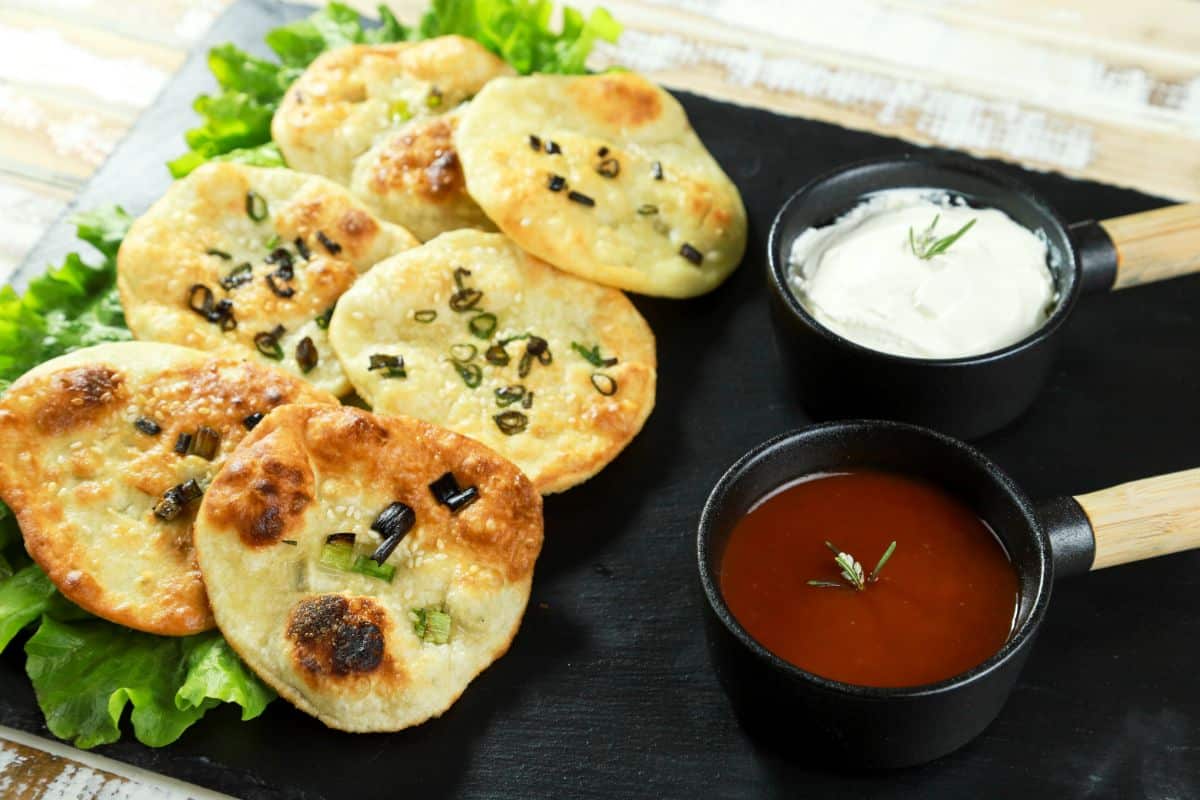 black platter of green onion dumpling chips next to bowls of dipping sauces