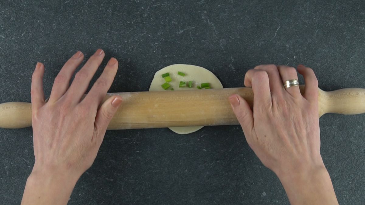 round dumpling being rolled out with wood rolling pin