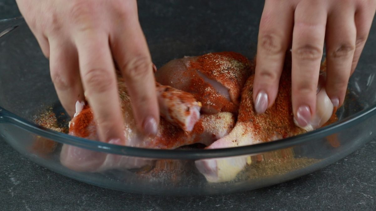 hands rubbing spices into chicken legs in baking dish