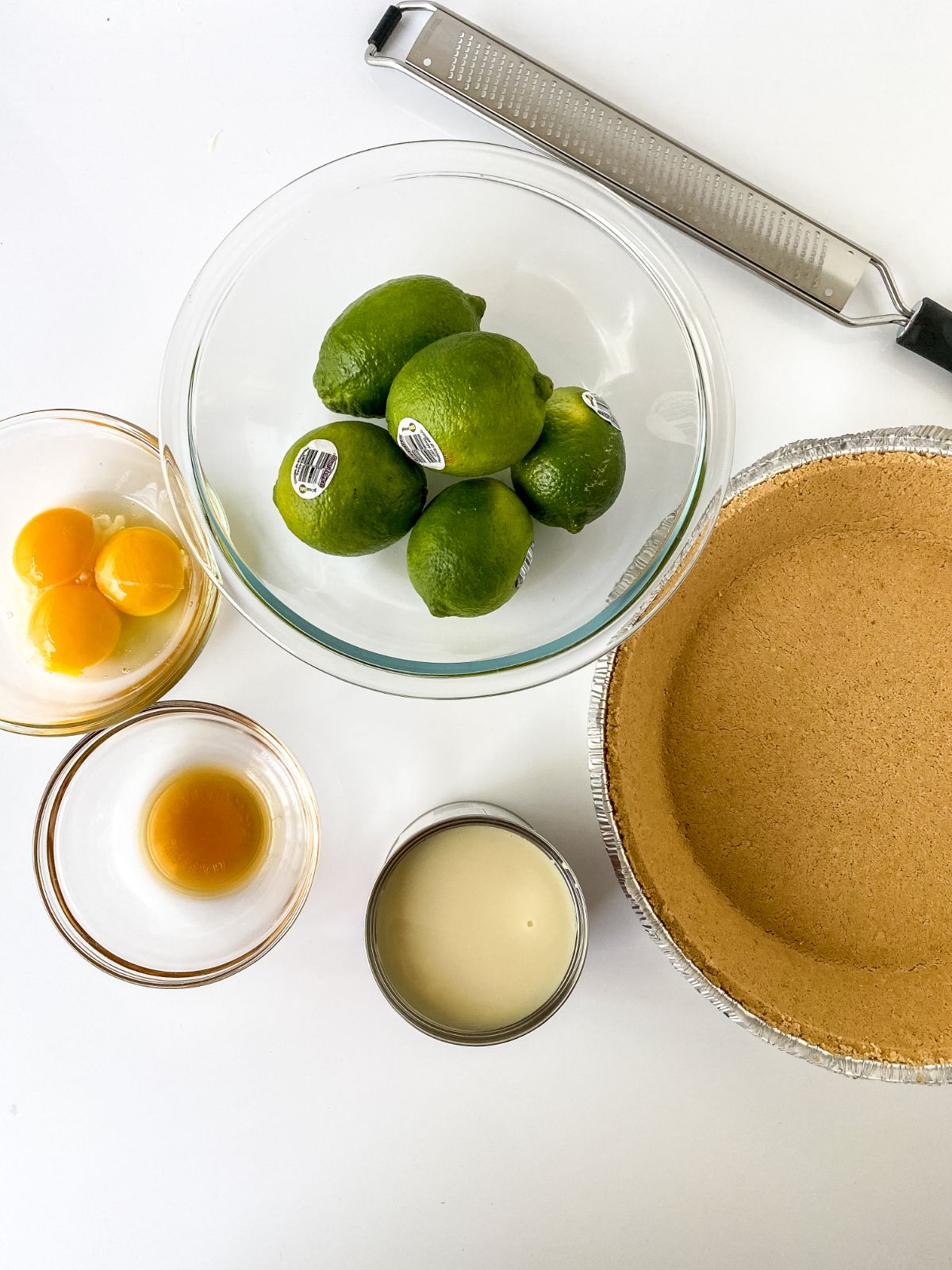 glass bowl of limes next to prepared graham cracker crust