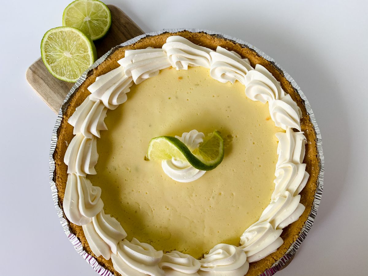 white table under key lime pie with halved limes beside pie