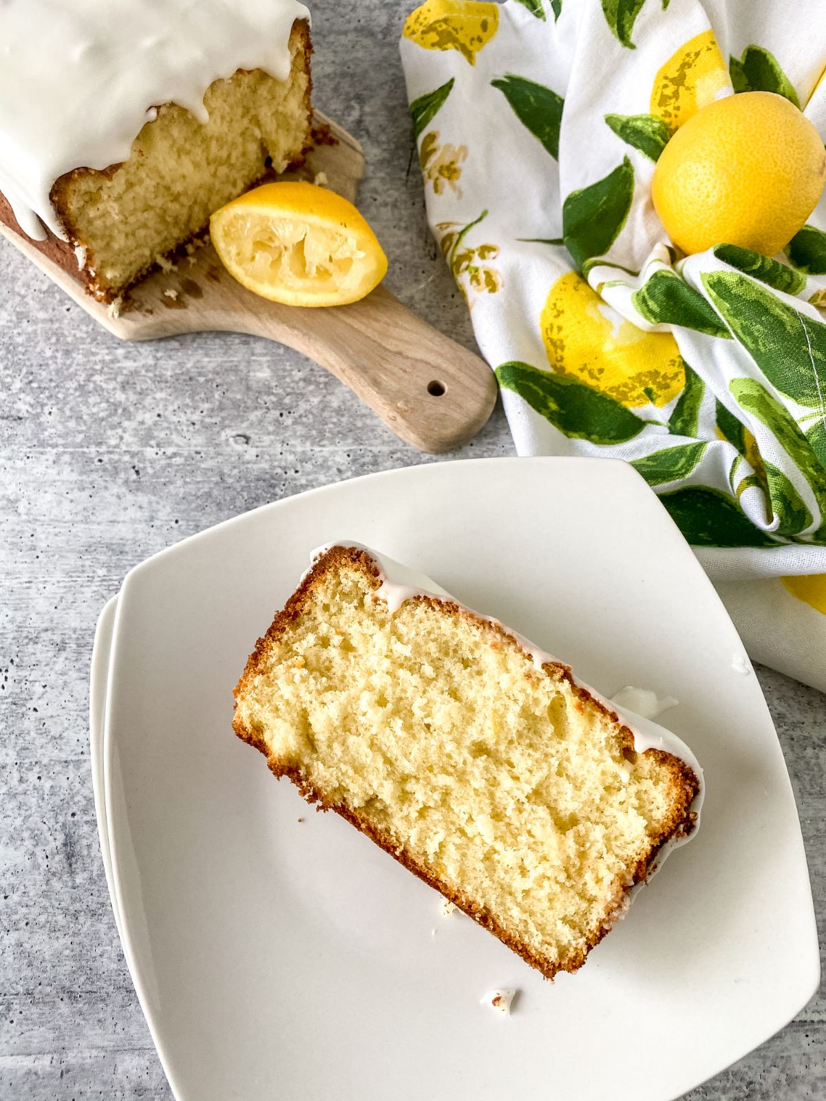 square white plate holding slice of lemon loaf next to floral napkin on table